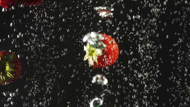 草莓掉进水中，黑色背景上有气泡。