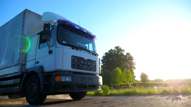 在日落時分行駛在高速公路上運送貨物的帶有拖車的卡車?？ㄜ囋诿利惖淖匀画h(huán)境中穿過鄉(xiāng)村公路。貨物運輸?shù)母拍?。慢鏡頭