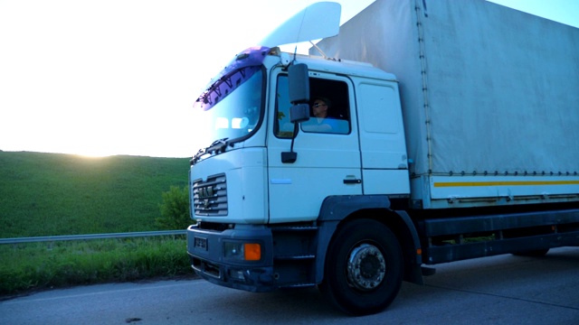 詳情圖-關(guān)閉卡車與貨運(yùn)拖車在公路上行駛和運(yùn)輸貨物。日落時(shí)分，一輛卡車在鄉(xiāng)間高速行駛。貨物運(yùn)輸?shù)母拍?。美麗的背景。慢鏡頭