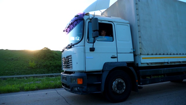 詳情圖-關(guān)閉卡車與貨運(yùn)拖車在公路上行駛和運(yùn)輸貨物。日落時(shí)分，一輛卡車在鄉(xiāng)間高速行駛。貨物運(yùn)輸?shù)母拍?。美麗的背景。慢鏡頭