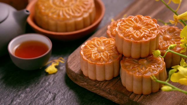 美麗的月餅在木托盤(pán)與茶和花在黑石板背景。中國(guó)傳統(tǒng)的中秋節(jié)觀念。