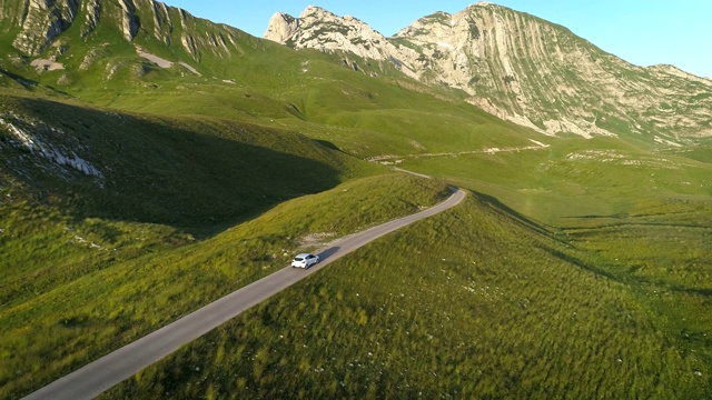 鸟瞰图的白色汽车行驶在山区蜿蜒的道路在日落的灯光。航拍4K无人机拍摄