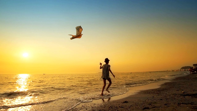 一个小男孩放着风筝在空旷的海滩上奔跑，背景是令人惊叹的夏日日落