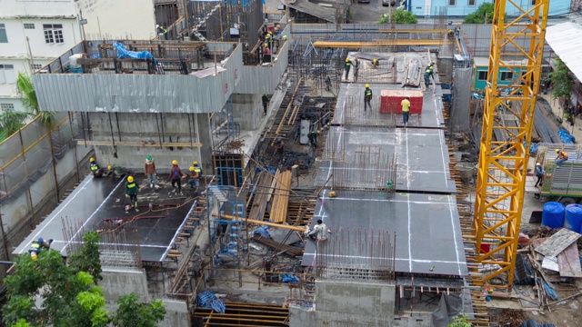 繁忙的工業(yè)建筑工地工人用起重機(jī)工作的鳥瞰圖。中午發(fā)展高層建筑大樓俯視圖。