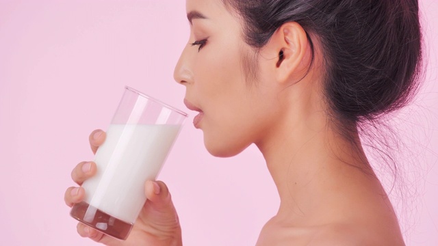 年轻快乐的女人喝鲜奶在粉红色的背景。清洁平衡的健康食品理念。健康饮食与健身理念。有机食品。医疗保健理念。视频:多样化的肖像