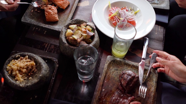 在餐館里享用美味的紅肉、魚(yú)、土豆、沙拉和飲料的陌生男女