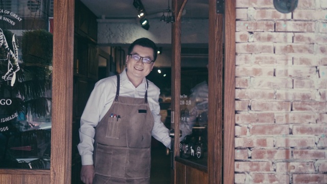 友好的亚洲男性经理打开鞋店的门，欢迎新客户