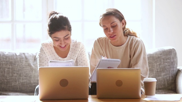 两个快乐的不同的女孩学生朋友一起在家里学习