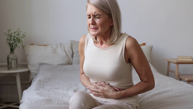 生病的成熟女人抱着肚子在床上感到腹痛