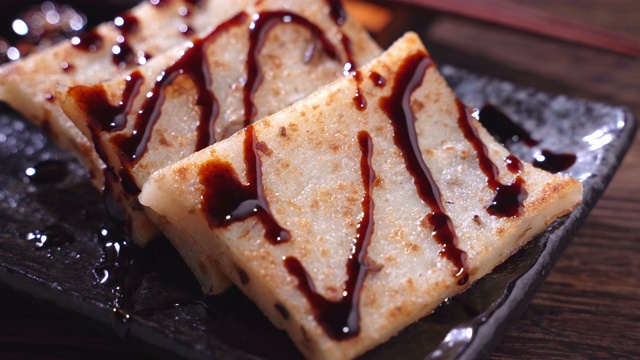 在餐厅将黑酱油倒在即食的美味萝卜糕上，这是中国传统的地方菜萝卜糕。