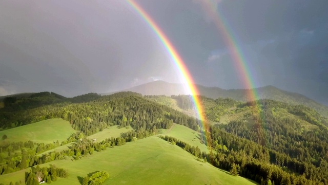 美丽的双虹移动在清新的绿色森林景观在阳光明媚的夏夜雨后空中