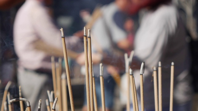 在中国农历新年的庆祝活动中，人们在道教寺庙内部祈祷和崇拜鞠躬和举香。室外的大壶，盛满了沙子，放在桌子上。特写镜头。4 k