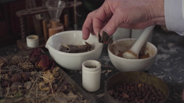 特写:白种人男性的手将干蝴蝶放入臼中，用杵研磨古药。医疗替代医学复古复古