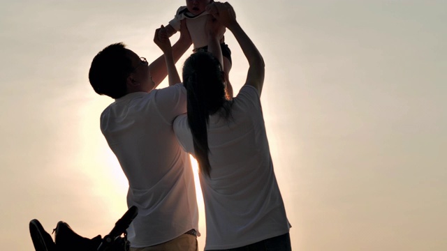 快乐的亚洲父亲，母亲和婴儿儿子愉快与乐趣沿海边的日落海浪在沙滩上。积极的父母和人在暑假与孩子户外活动。幸福的家庭假期。家庭、生活方式、人、人寿保险、假期