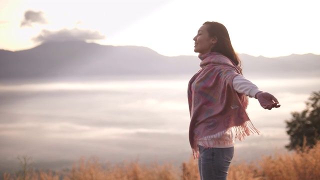 自由亚洲女人站在山顶，张开双臂，欣赏日落