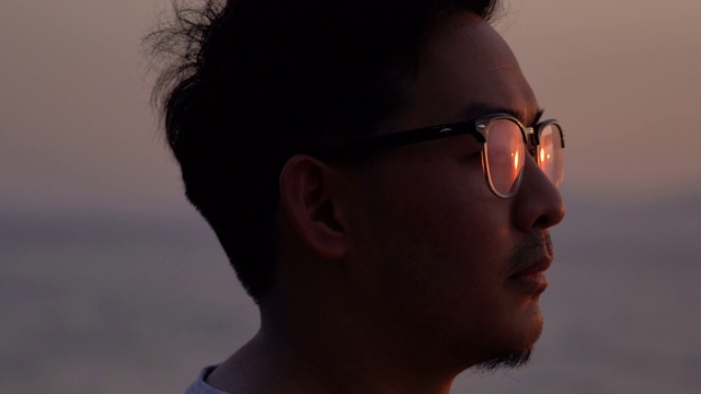 特写脸的亚洲人在眼镜看日落与阳光反射