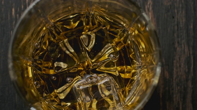 威士忌从棕色瓶子倒进玻璃杯。前视图。浇注波旁威士忌