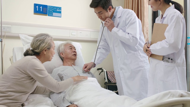 年轻的亚洲医生在医院病房检查老年病人