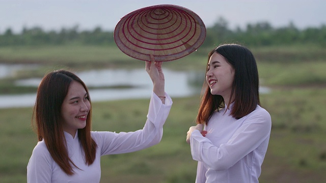 一位美丽的年轻女子穿着一件白色的连衣裙，拿着一顶竹编织的帽子。站着对着镜头笑，心情很好
