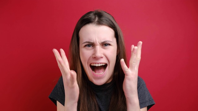 有攻击性的沮丧女人愤怒地大喊大叫，握紧拳头，表达愤怒，准备打敌人，穿着灰色t恤，孤立在红色背景。女士要为自己站起来