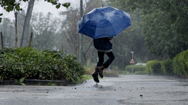 一个小男孩拿着伞在倾盆大雨中跳跃的慢动作