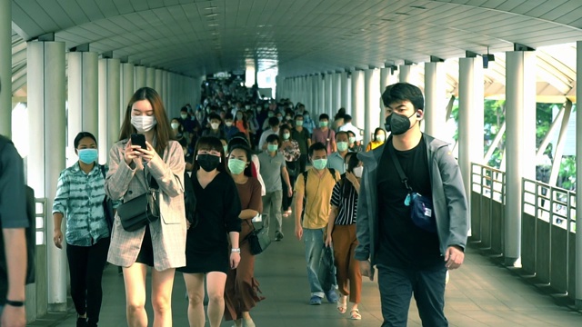 在泰国曼谷的崇诺寺BTS车站，下班高峰期，许多人戴着面具走在大桥上的慢镜头。