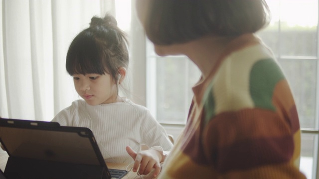 年轻的母亲在家里帮助小女孩做作业。
