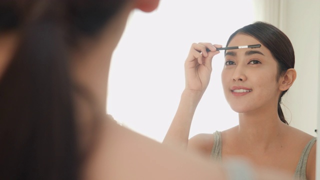 美女化妆刷用粉状化妆品涂抹面部肌肤。快乐自信的亚洲美丽的年轻女子化妆用粉敷在脸上在镜子在家里早上。