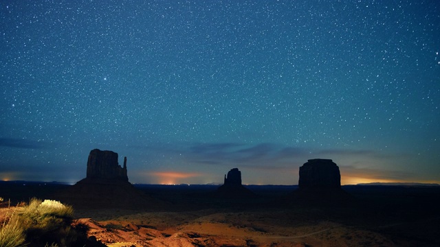 星星和流星的时间流逝在夜空与岩石的轮廓在远处在犹他州/亚利桑那州的纪念碑谷沙漠在晚上
