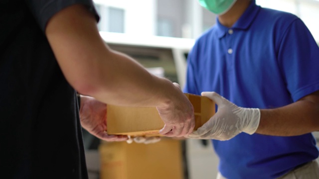 近距离观察亚洲蓝色快递员戴医用橡胶手套送包裹给客户，在发货前。4k分辨率和慢动作拍摄。