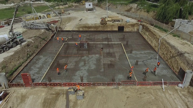 一群建筑工浇筑混凝土。在一个大型建筑工地的地基上，建筑商正在建造摩天大楼或工厂。在建筑工地工作的工人。