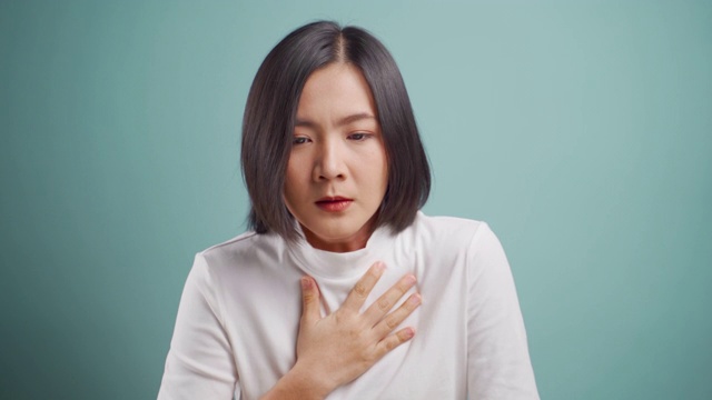 一名亚洲妇女病了，气喘吁吁，孤立地站在蓝色背景上。卫生保健的概念。4 k的视频。