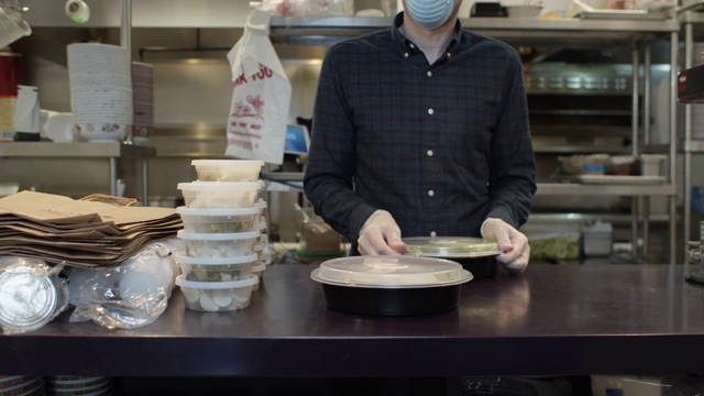 2019冠状病毒病爆发期间，戴手套和面罩的餐馆老板将食物装箱供外卖