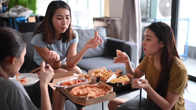 3位亚洲华人女性朋友在客厅吃披萨作为午餐