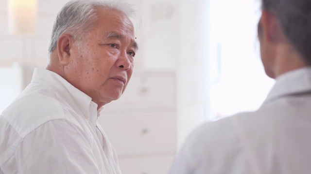 詳情圖-亞裔老年男子聽著年輕的黑人女護士醫(yī)生在家給他年長的男性病人咨詢。采購產(chǎn)品醫(yī)療，護理，護理，退休，志愿者，慈善，教育，養(yǎng)老院，在家照顧者，醫(yī)藥和衛(wèi)生保健