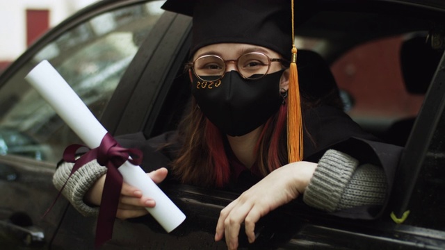 十几岁的女孩穿着毕业礼服和帽子和防护面具与文凭在车里