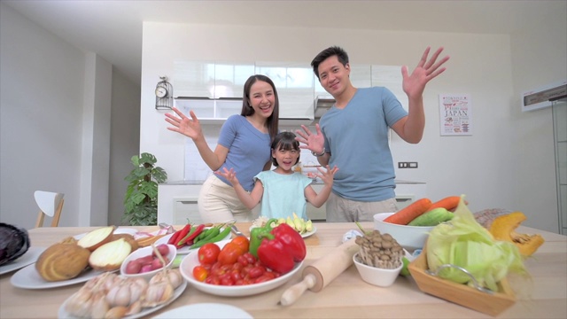 在白色整洁的厨房里，亚裔家庭和女儿向镜头挥手问好的慢动作镜头