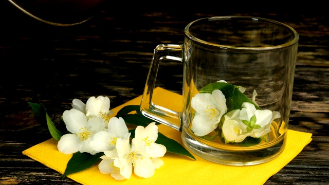 准备茉莉花茶。新鲜的茉莉花花瓣和鲜花被扔进玻璃透明的茶杯里。