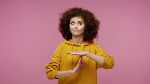 詳情圖-疲憊的女孩非洲發(fā)型在帽衫看著懇求受驚的眼睛和顯示出時間出手勢