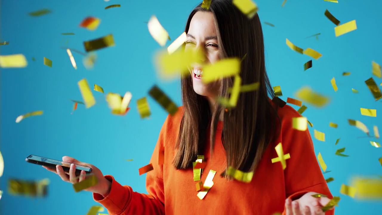 詳情圖-慶祝一位手持手機(jī)獲獎的年輕女性，并在演播室里灑上金色的五彩紙屑