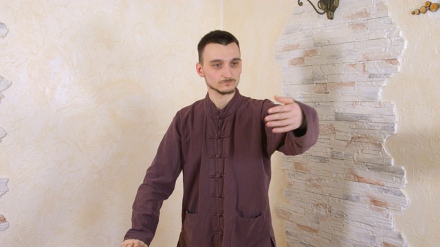 年轻男子练习太极拳体操在岩石墙的背景。健身的人穿着中国传统服装练气功。