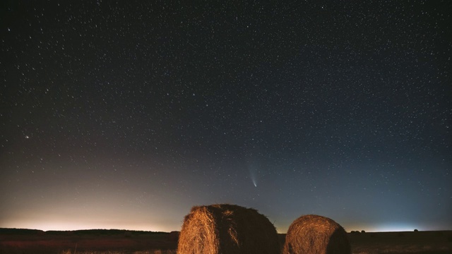 彗星Neowise C/2020 F3在夜晚星空在夏季农业领域的草垛上。夜晚的星星与收获后的干草捆的乡村景观。农业的概念。FullHD间隔拍摄