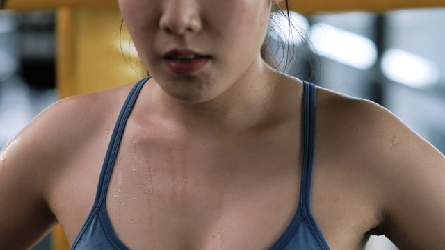 近距离慢动作:运动的年轻亚洲女性疲惫的汗水在她的身体休息后，健身房锻炼。运动员在高强度的运动后，在体育馆休息，看向远处，这是健康的生活方式概念。
