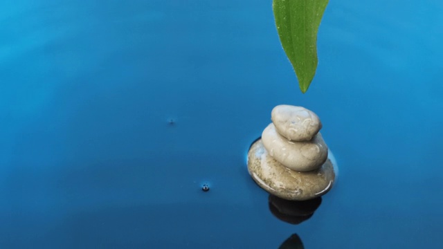 水滴落在金字塔上，綠葉落在藍色的水中。水療中心的背景。