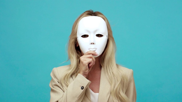 自信的金发中年妇女在商务风格夹克脱下面具显示不同的情绪，表里不一，虚伪