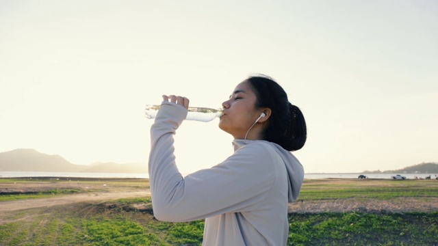 年轻的亚洲女人跑步喝水后在户外的山。