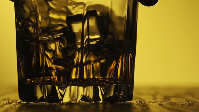 在玻璃杯中旋转冰块的威士忌。手持金色的威士忌酒杯