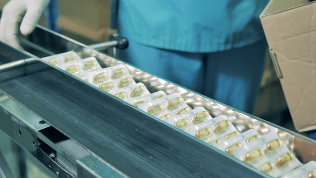 工厂工人正在用药丸从皮带上取下水泡