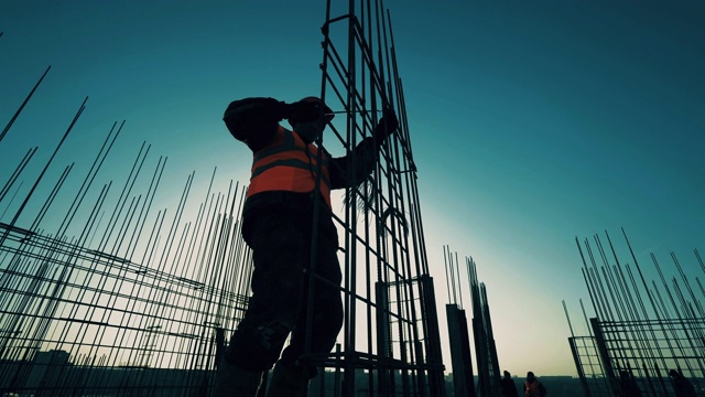 工人正在建筑顶部建造金属骨架。建筑行业，建筑项目，日落时的建筑过程。