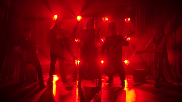 演播室里的摇滚乐队演奏着以红灯为背景的歌曲。时髦的女歌手用麦克风唱歌，男人们演奏乐器。剪影。慢动作
